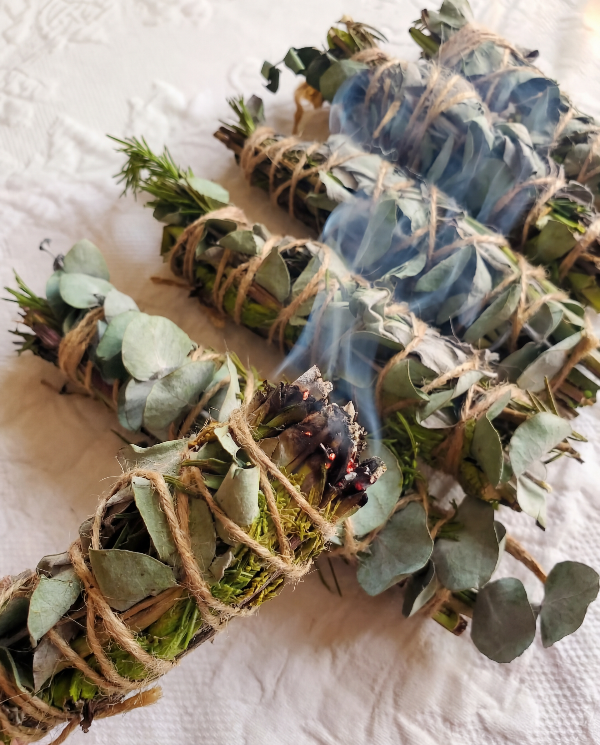Three smudge sticks with leaves and twine on a white fabric background
