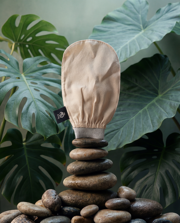 Beige Moroccan silk exfoliating glove on stone pedestal with monstera leaves