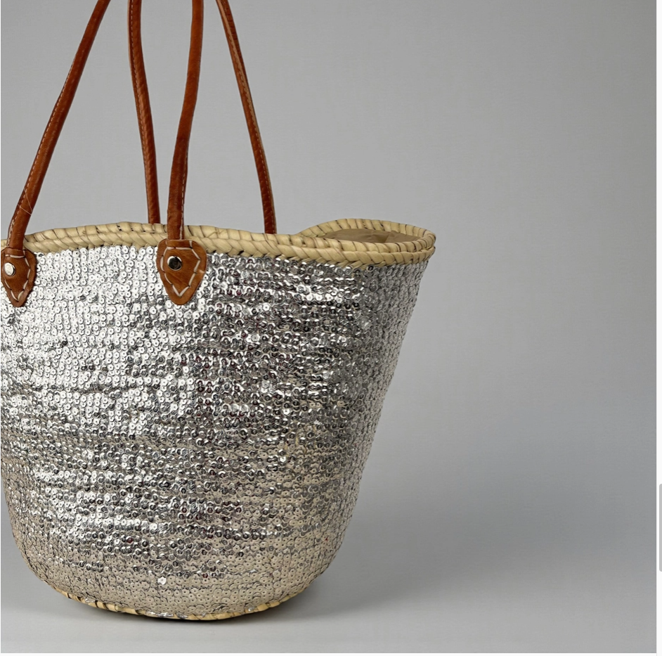Silver woven basket with brown leather handles on a gray background